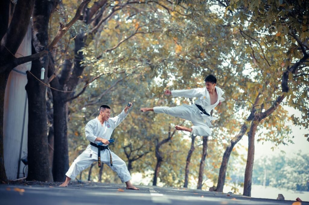 Two martial artists practicing kicks outdoors with trees in the background